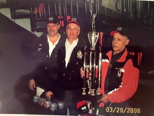 Three coaches holding a championship trophy at the rink, dated March 29, 2006