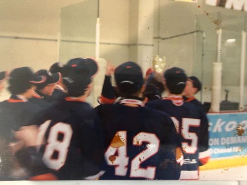 Players in dark jerseys huddled together on the ice with sticks raised